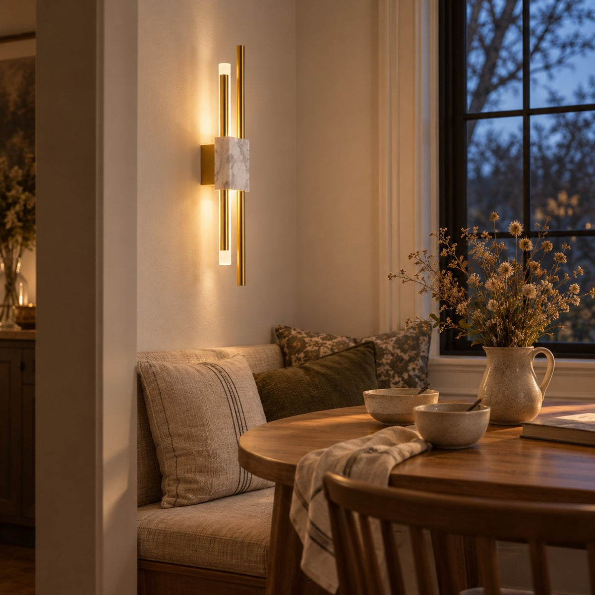 Alcochete asymmetric wall sconce with a white marble accent lit above a breakfast nook bench at dusk.