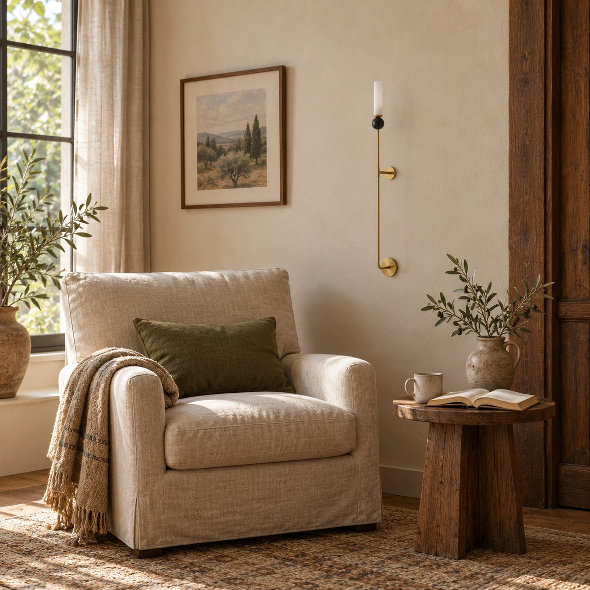 Aljezur vertical marble wall sconce on a brass rod beside a linen armchair in a sunlit living room.