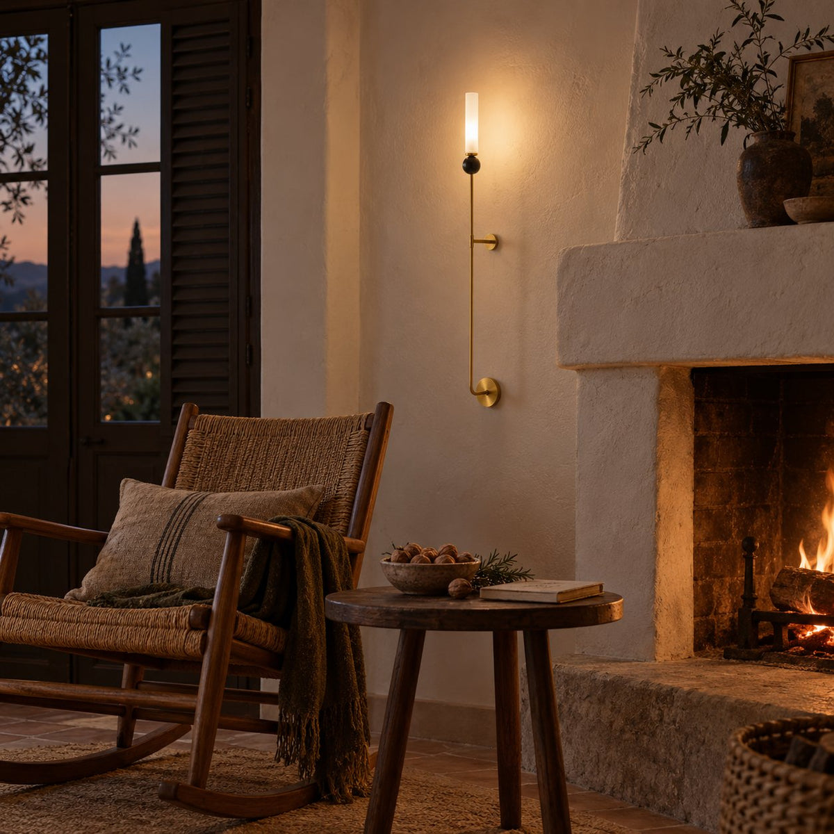 Aljezur tall brass wall sconce with a marble ball and frosted cylinder beside a lit fireplace.