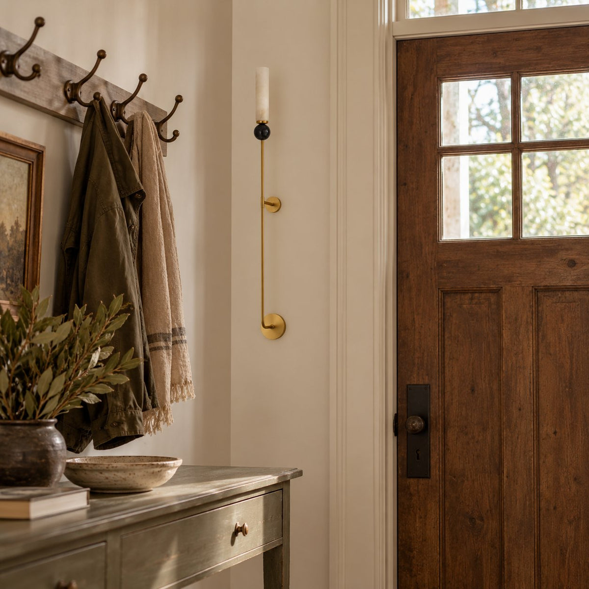 Aljezur wall sconce with a white marble shade, black ball accent, and brass rod in an entryway.