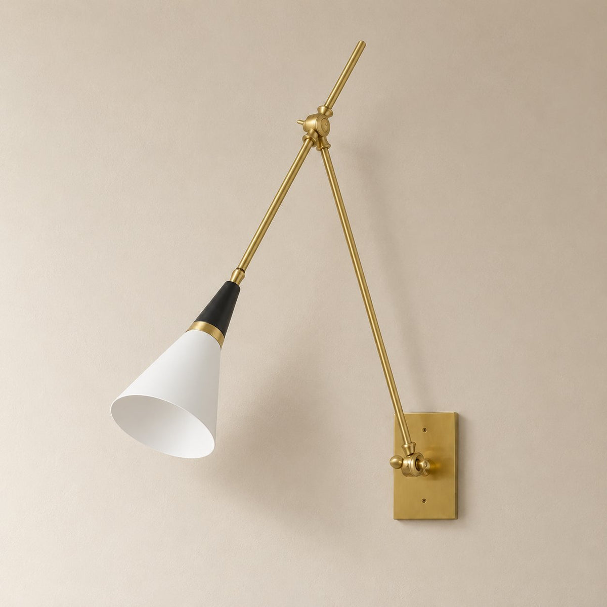 Almodôvar adjustable swing arm sconce in white, black and brass, unlit on a plain plaster wall.
