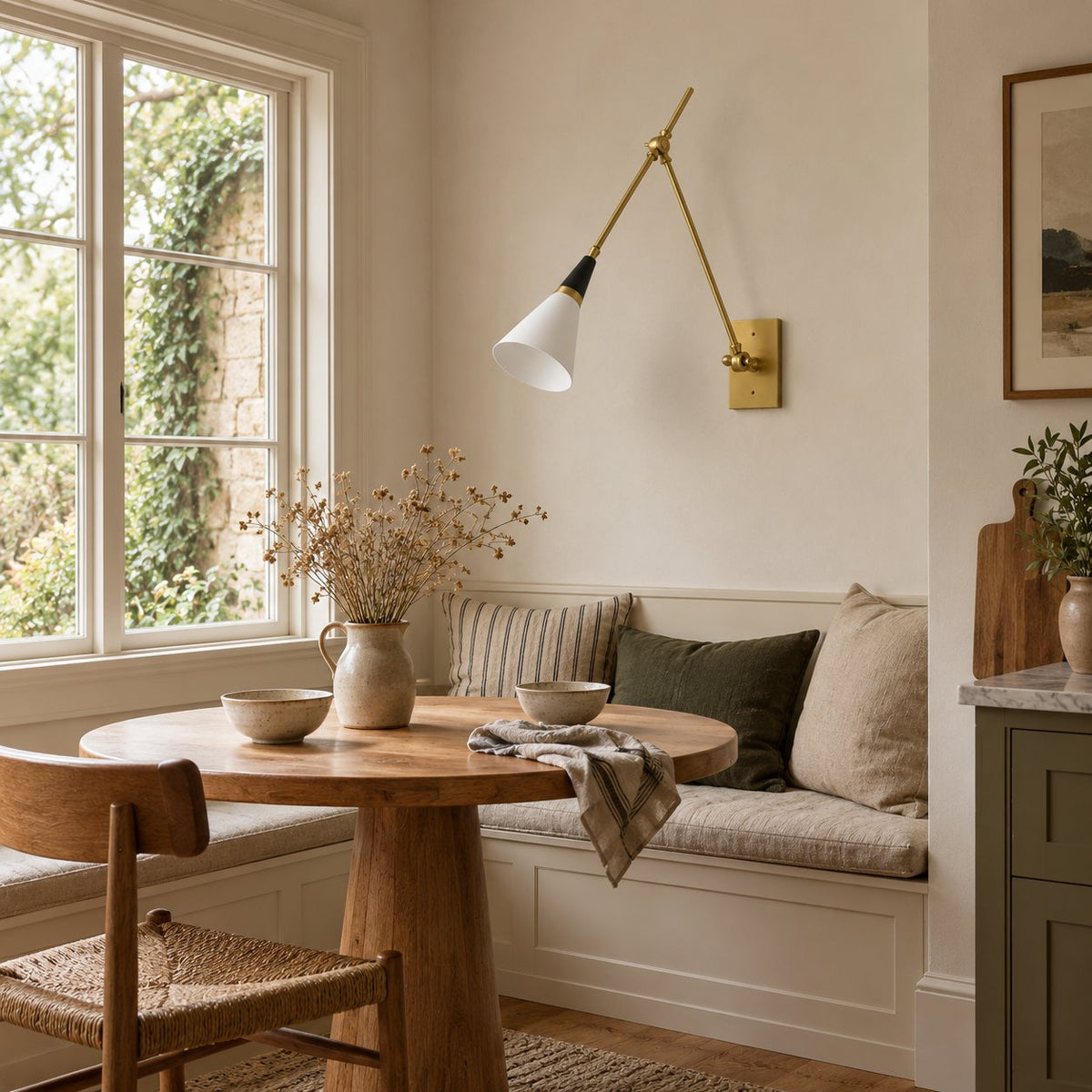 Almodôvar brass swing arm sconce with a white cone shade above a breakfast nook bench.