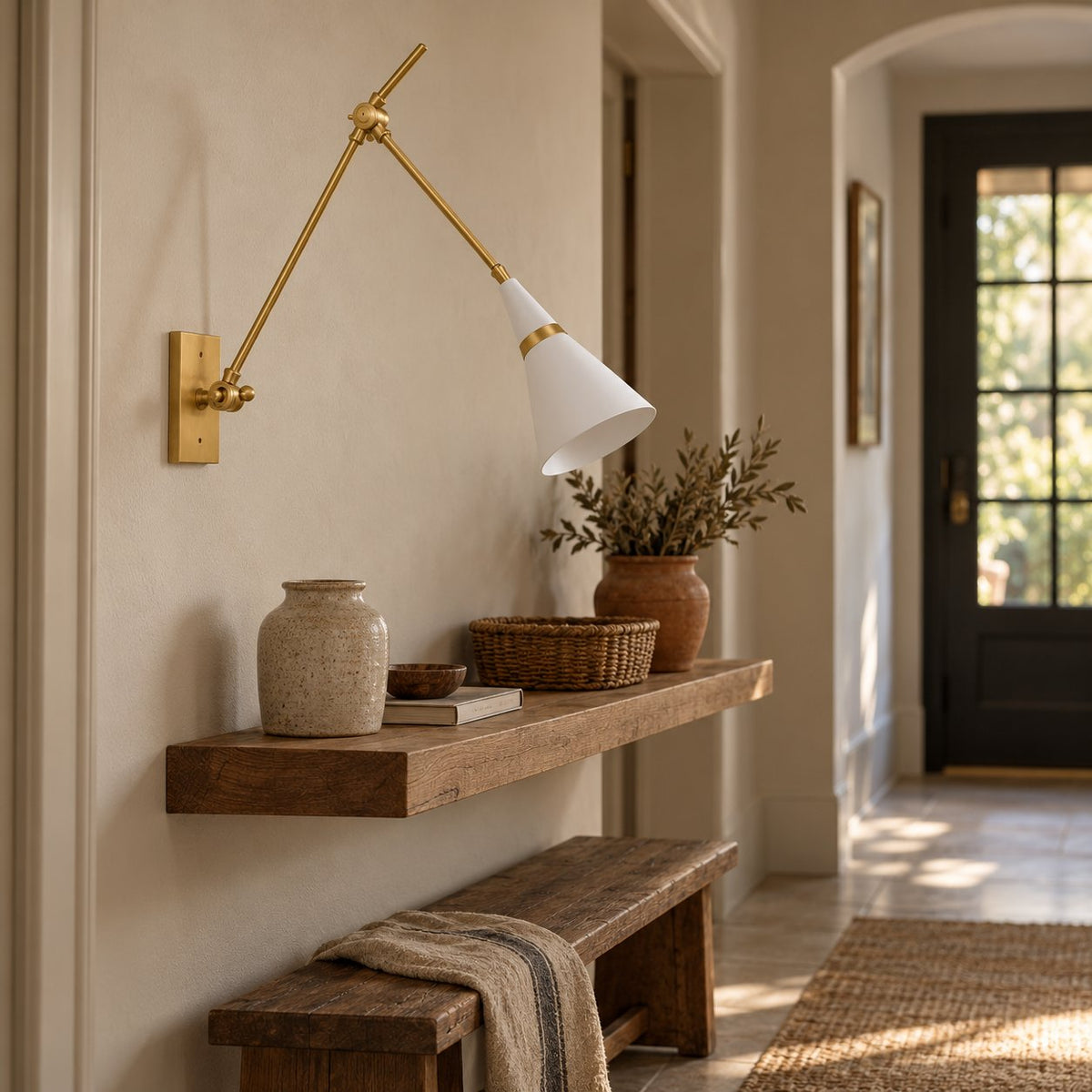 Almodôvar brass swing arm sconce with a white and brass cone shade above a hallway console shelf.