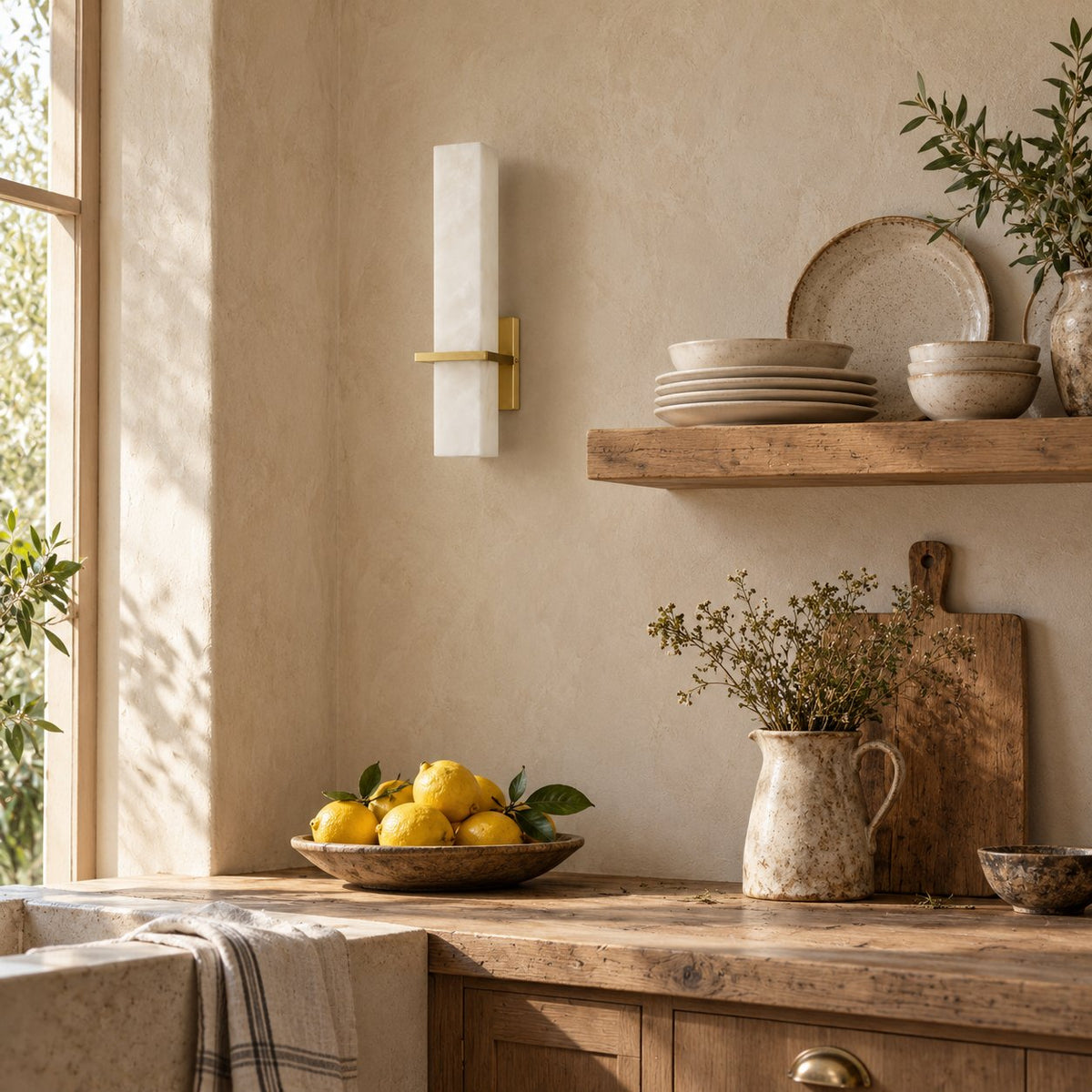 Amieira alabaster wall sconce with brass arm beside open kitchen shelving.