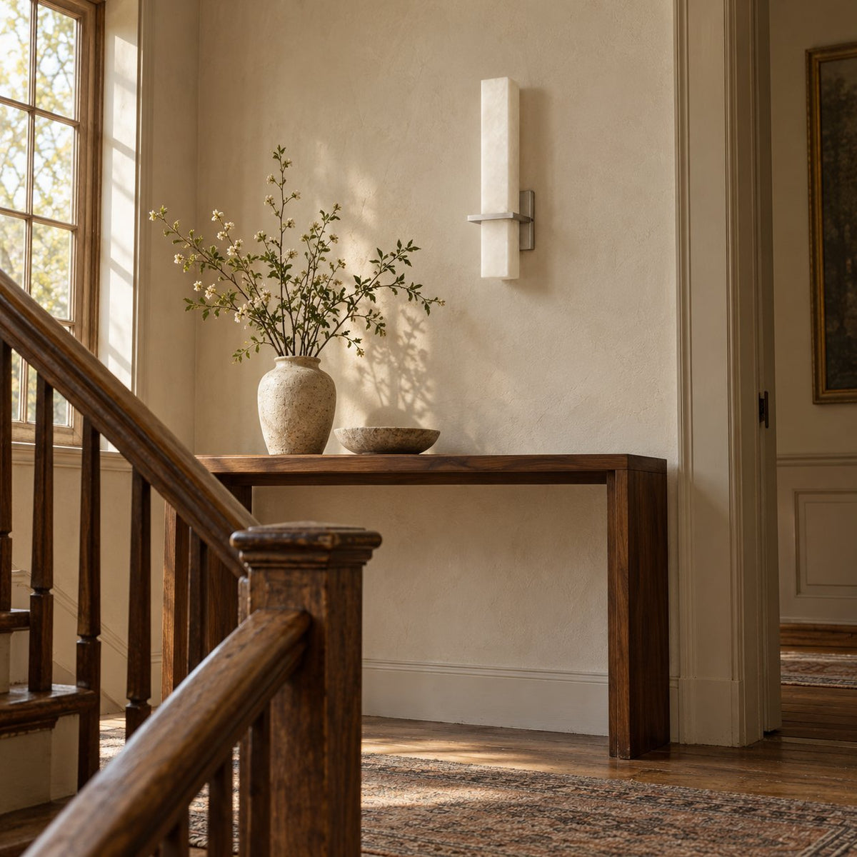 Amieira alabaster wall sconce with nickel arm beside a staircase console.
