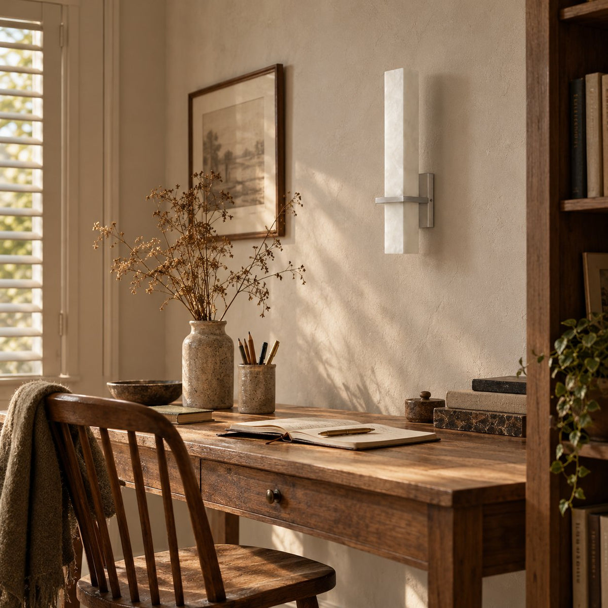 Amieira alabaster wall sconce with nickel arm above a wooden writing desk.