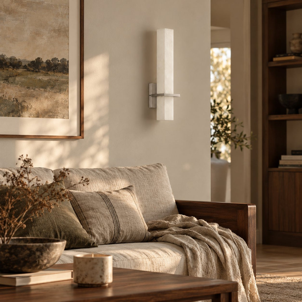 Amieira alabaster wall sconce with nickel arm beside a linen sofa and bookshelf.