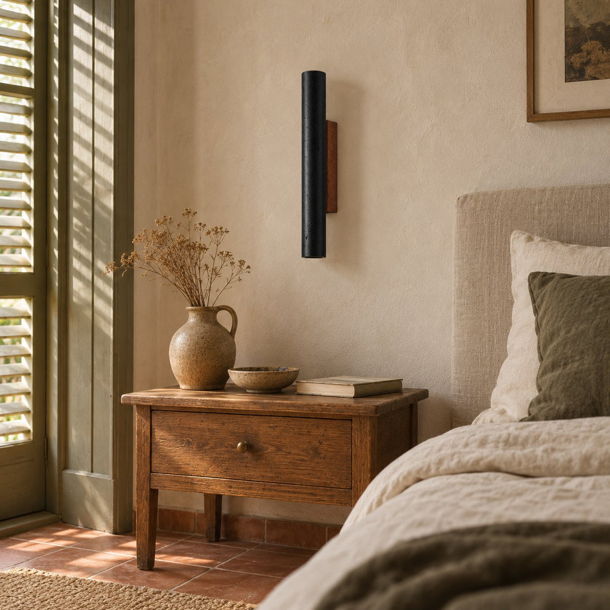 Arraiolos black travertine wall sconce with walnut back beside a bedroom nightstand.