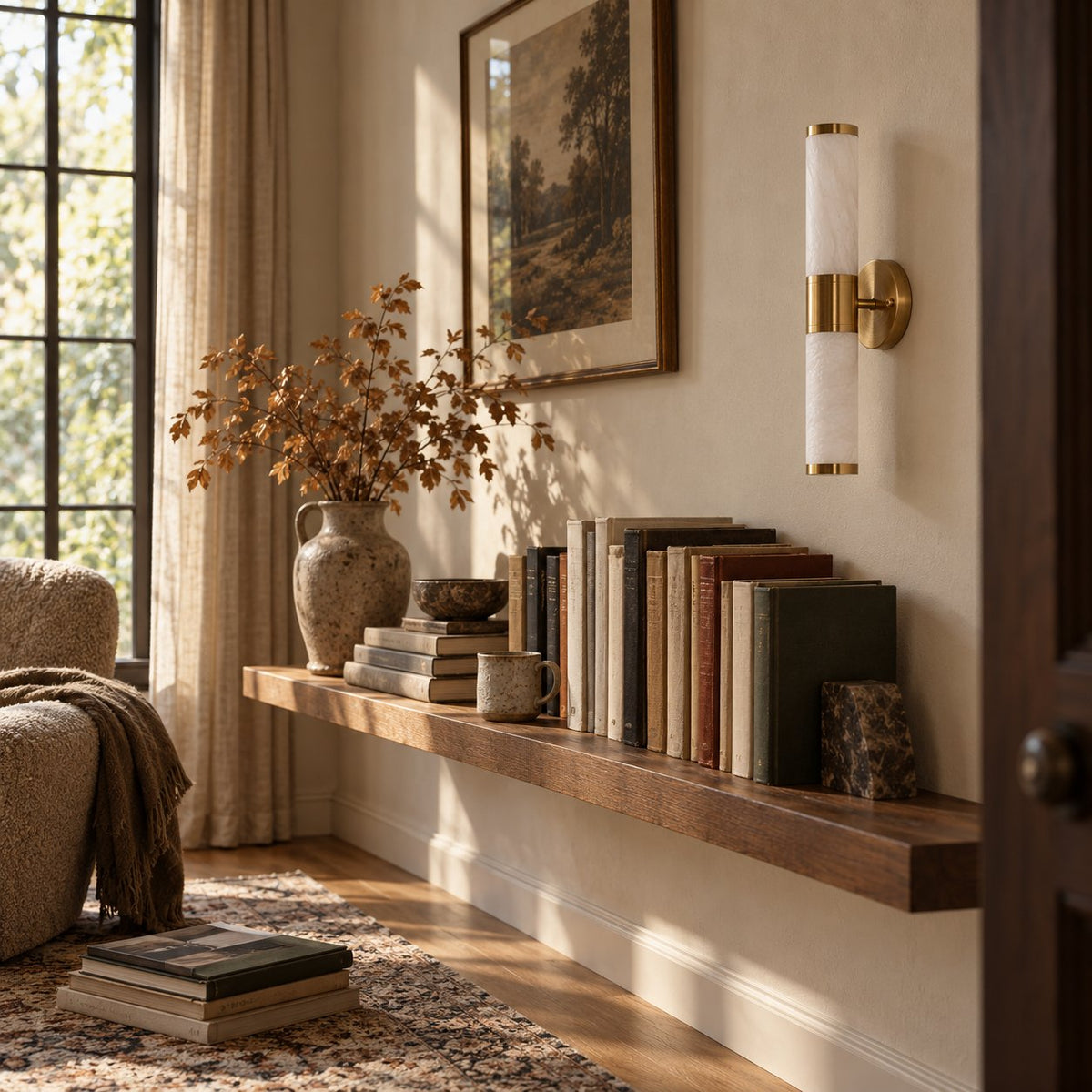 Beja alabaster wall sconce, a white cylinder with brass caps, above a wood shelf of books.