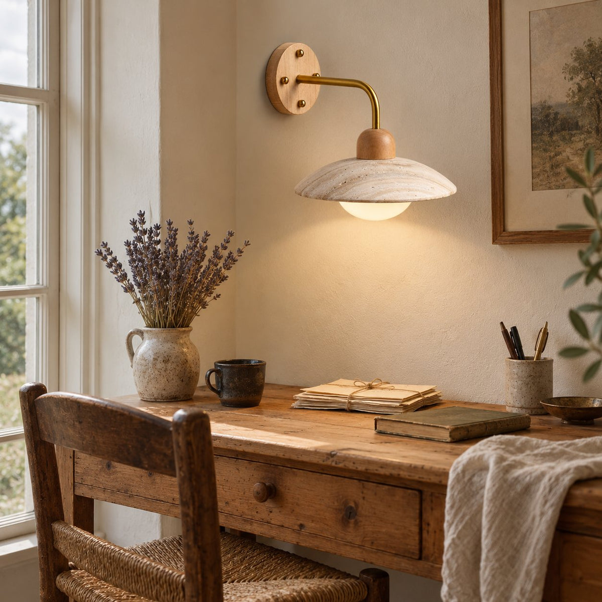 Boticas dome arm sconce in travertine with a brass arm, lighting a rustic writing desk.