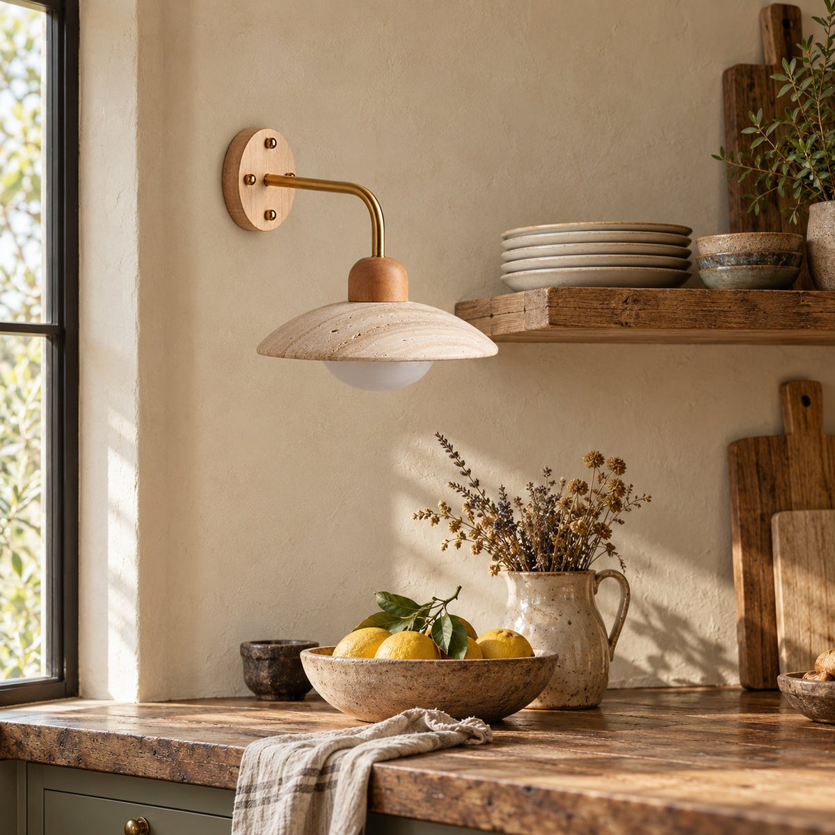 Boticas dome arm sconce in travertine with a brass arm, lighting a kitchen counter with lemons.
