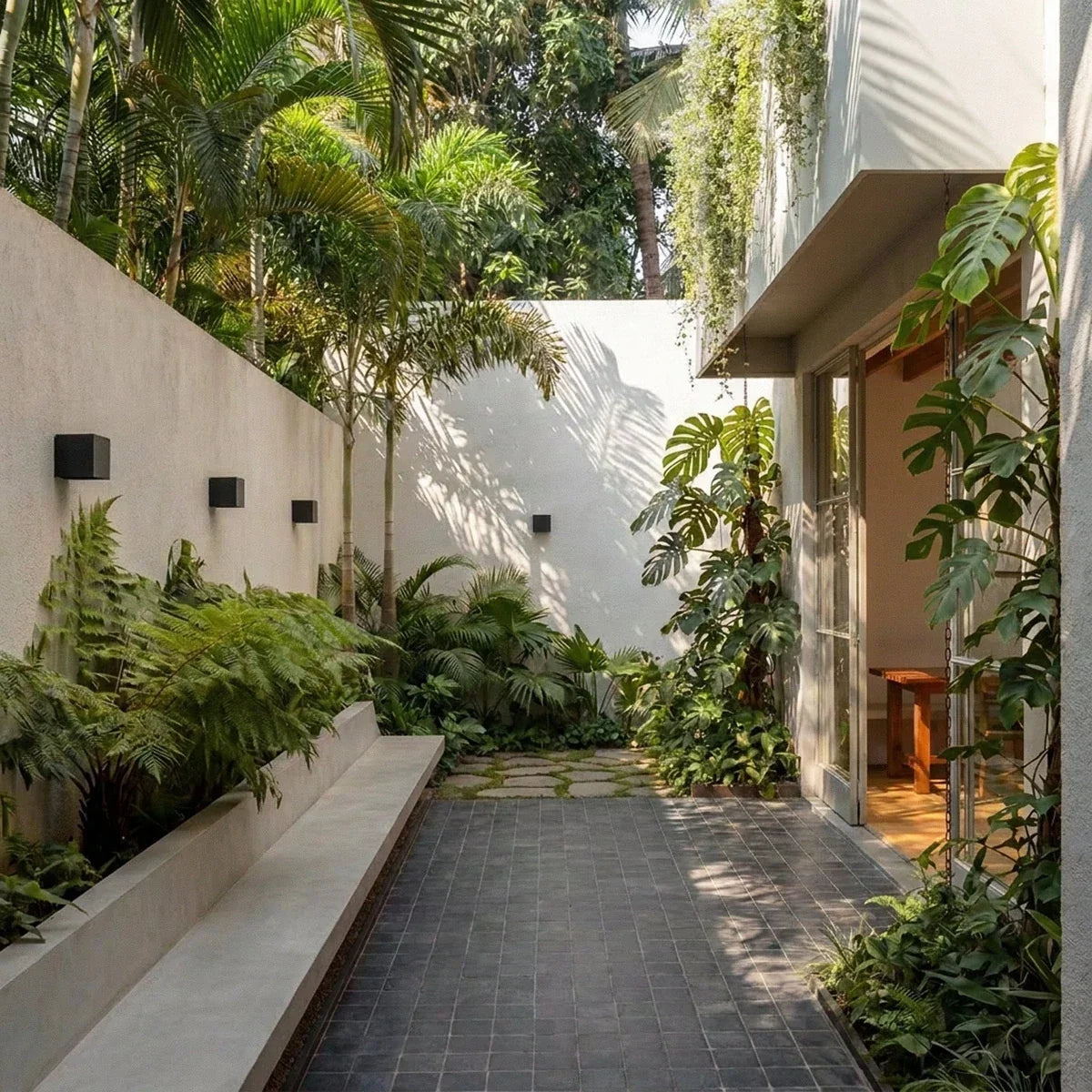 Four Clérachic black cube wall lights along a pale garden wall by a stone bench and ferns, seen in daylight beside a glazed door.