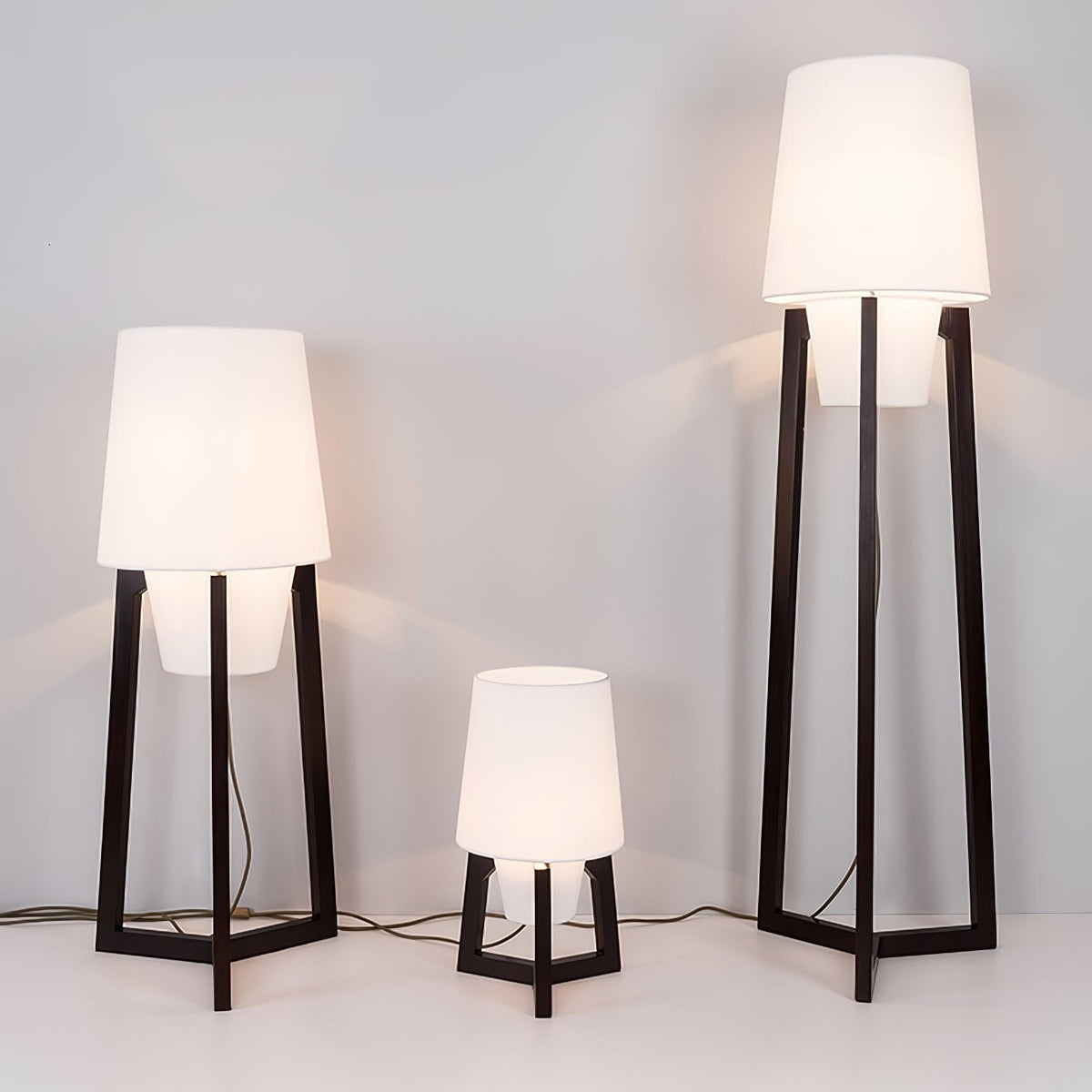 Morros floor lamps, three heights lit against a dark wall, wide view