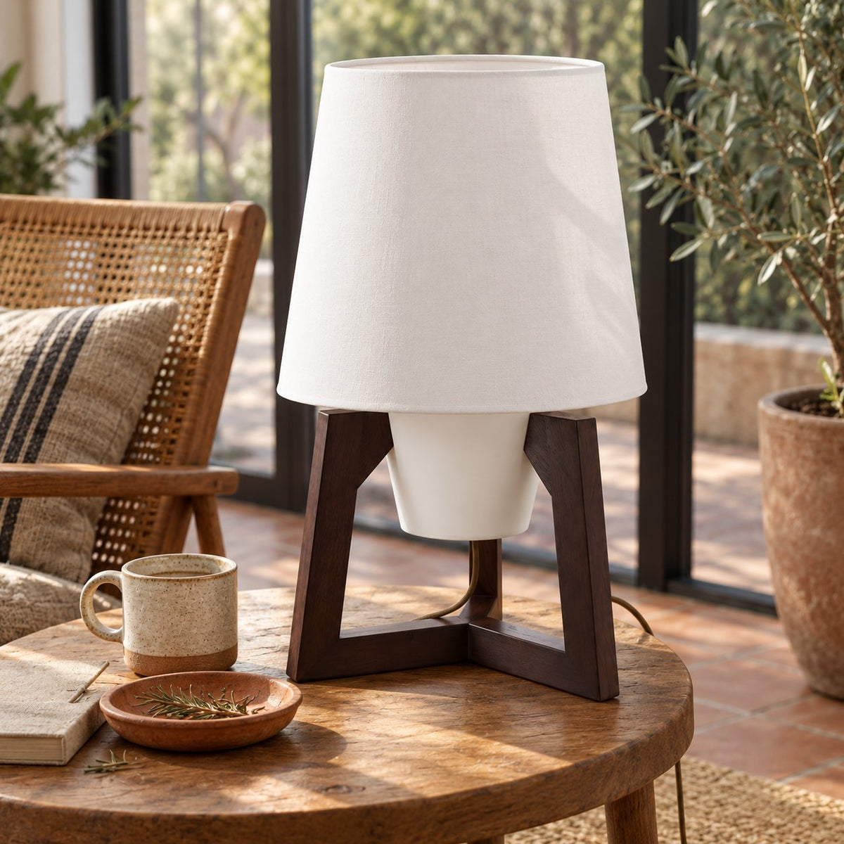 Morros small tripod linen table lamp in black walnut on a round wood side table in a garden room.