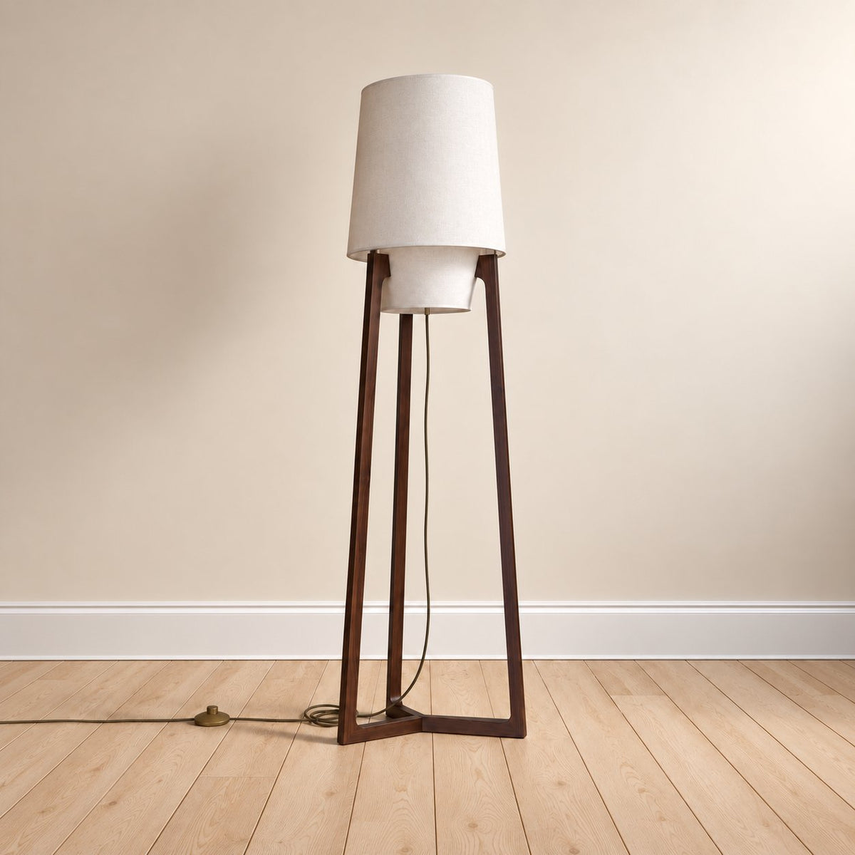 Morros tripod linen floor lamp in brown walnut, the 165 cm (65 in) size, cord to a brass foot switch, on an oak floor.