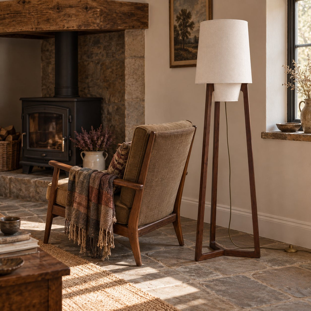 Morros tripod linen floor lamp in brown walnut, 165 cm, beside a lounge chair by a wood stove.