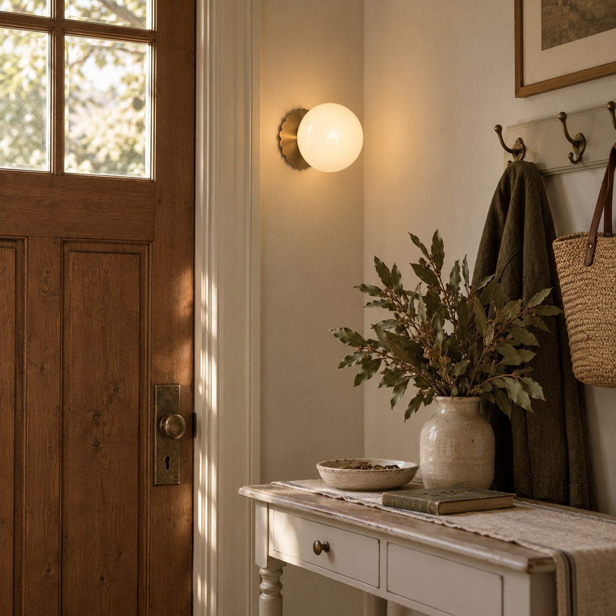 Tâmega convertible wall sconce in gold with beige glass above a painted console by a timber front door.