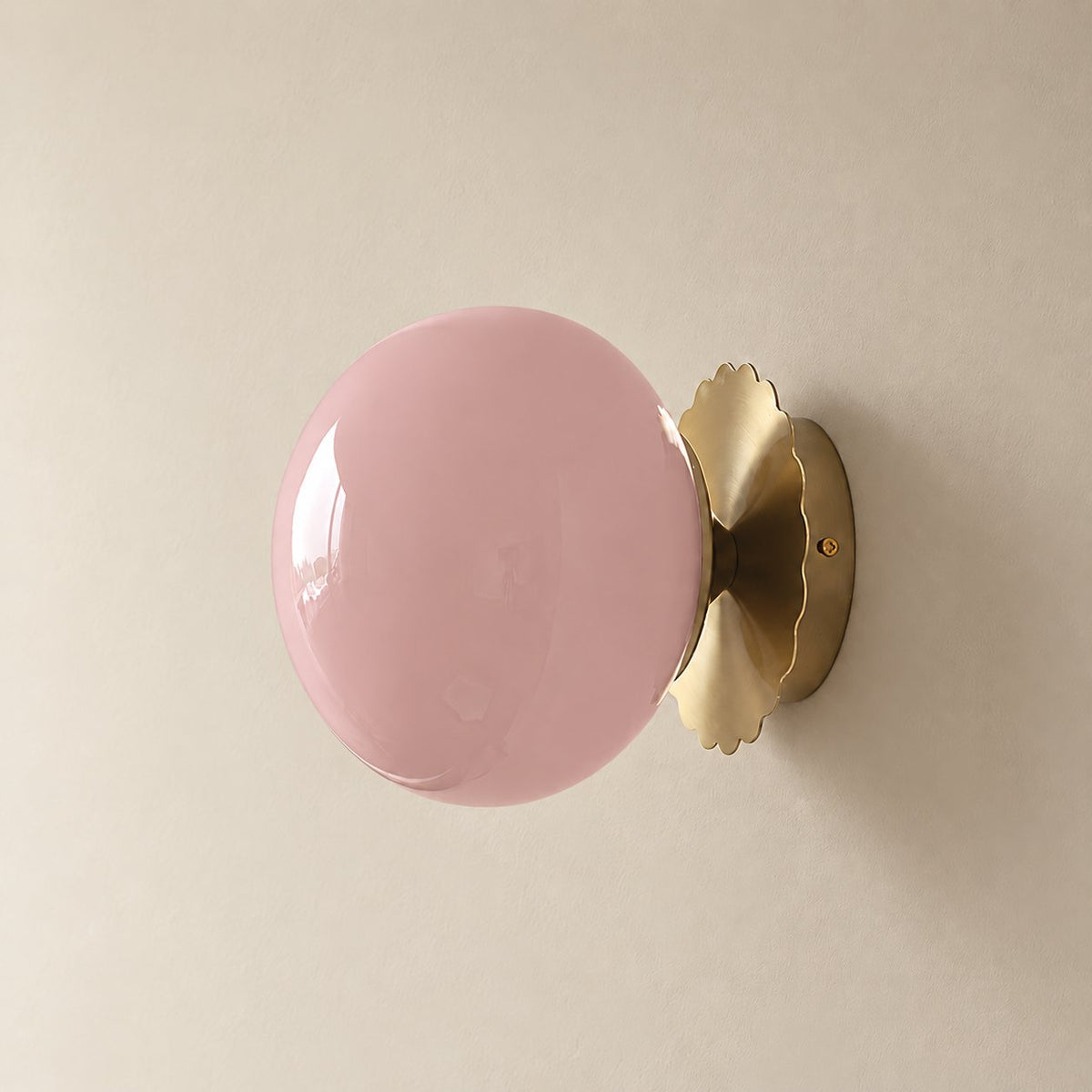 Tâmega convertible wall sconce in brushed brass with soft pink glass, unlit on a plain plaster wall.