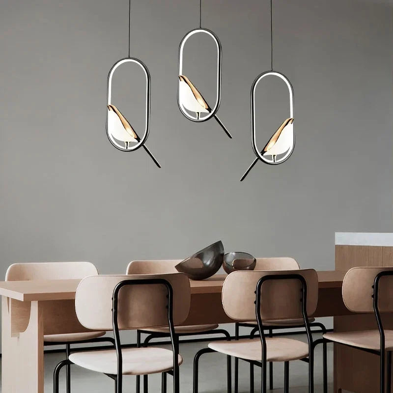 Three oval bird pendants at different heights over a dining table with wood chairs