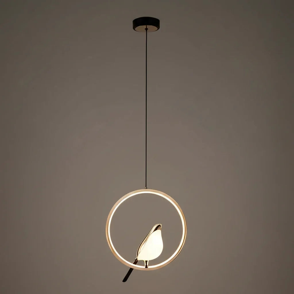 Gold ring frame bird pendant glowing against a taupe wall