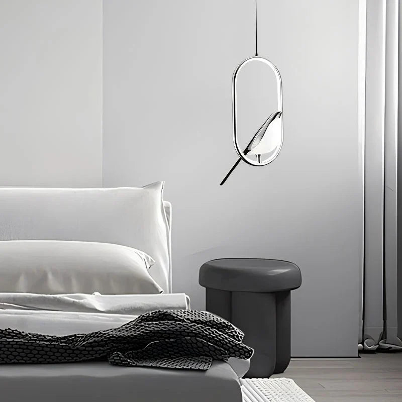 Silver oval bird pendant hanging beside a bed with gray bedding