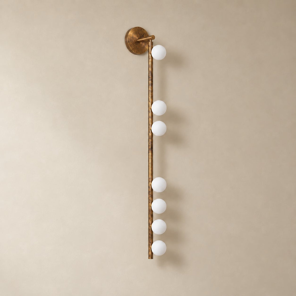Vouga glass tube wall sconce in antique brass, 7 heads B, 100 cm, unlit on a plain plaster wall.