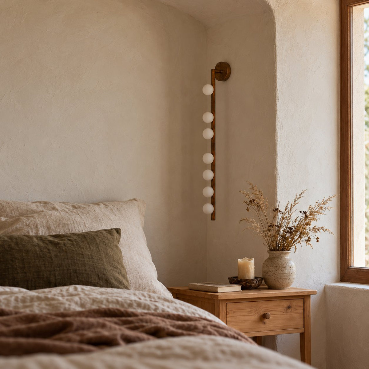 Vouga brass glass globe wall sconce with seven heads in a plaster alcove beside a linen bed.