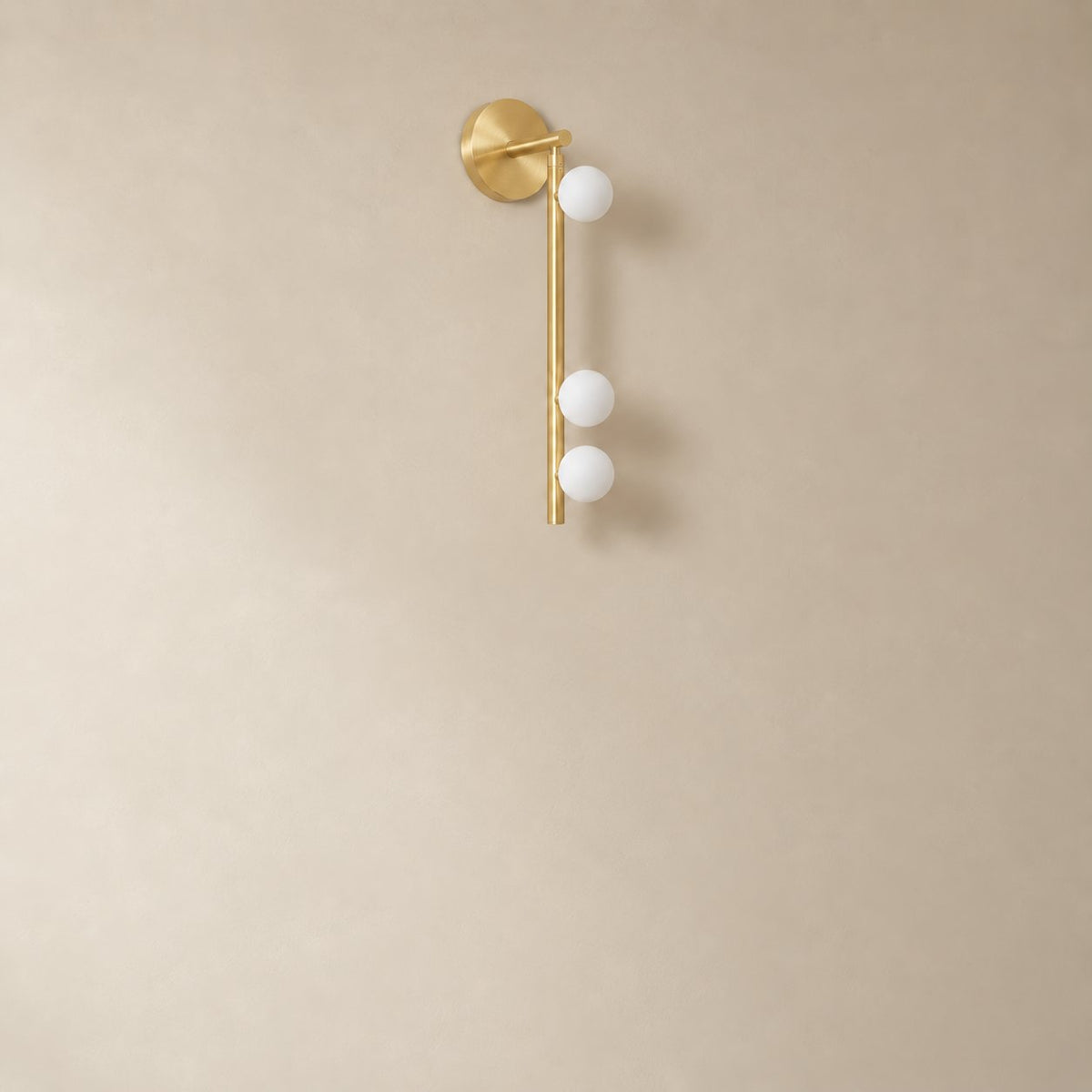 Vouga glass tube wall sconce in brushed brass, 3 heads, 50 cm, unlit on a plain plaster wall.