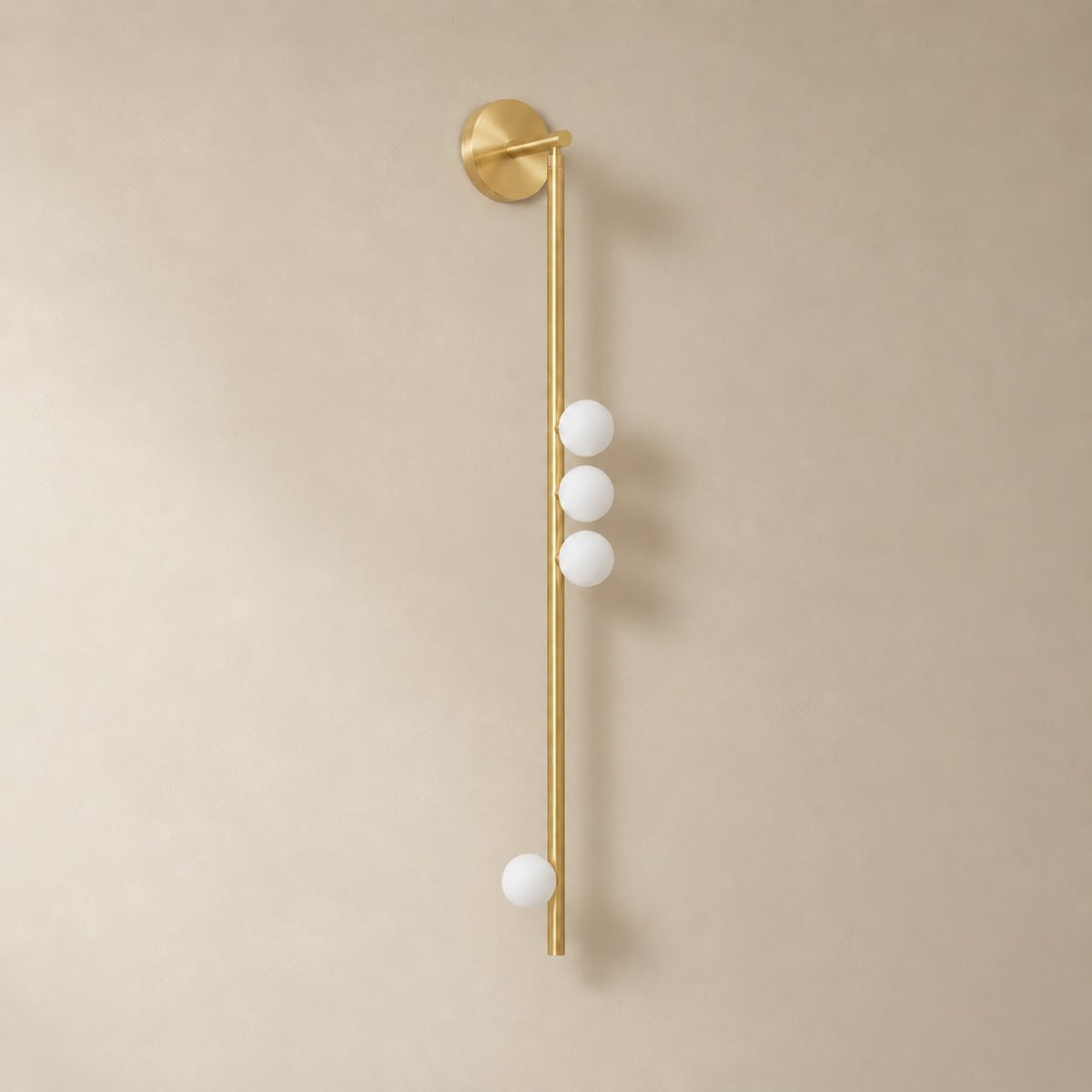 Vouga glass tube wall sconce in brushed brass, 4 heads, 100 cm, unlit on a plain plaster wall.