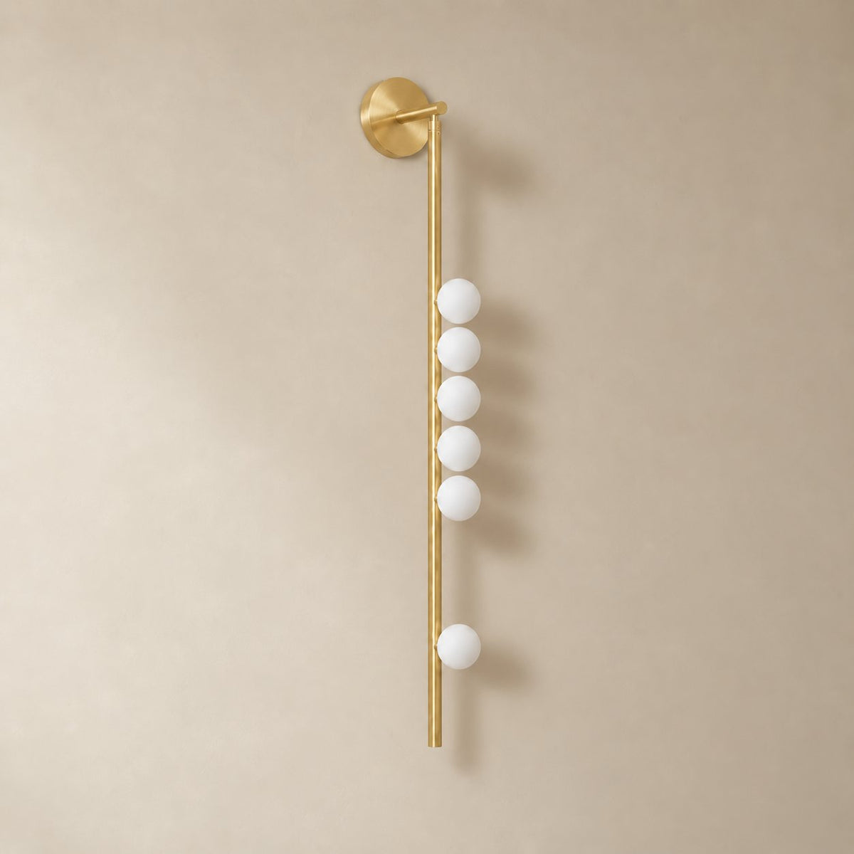 Vouga glass tube wall sconce in brushed brass, 6 heads, 100 cm, unlit on a plain plaster wall.