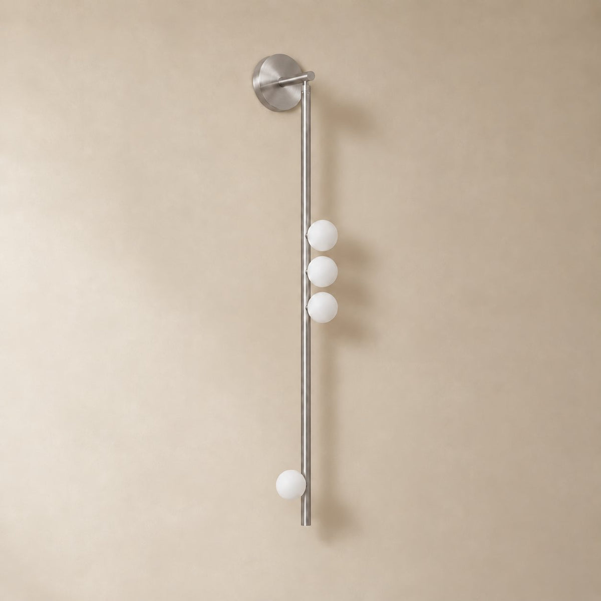 Vouga glass tube wall sconce in brushed nickel, 4 heads, 100 cm, unlit on a plain plaster wall.