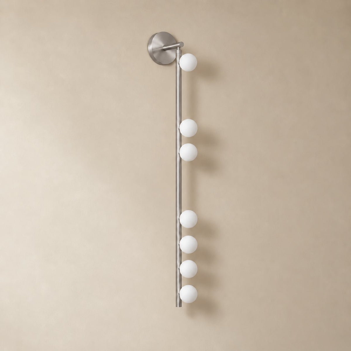 Vouga glass tube wall sconce in brushed nickel, 7 heads B, 100 cm, unlit on a plain plaster wall.
