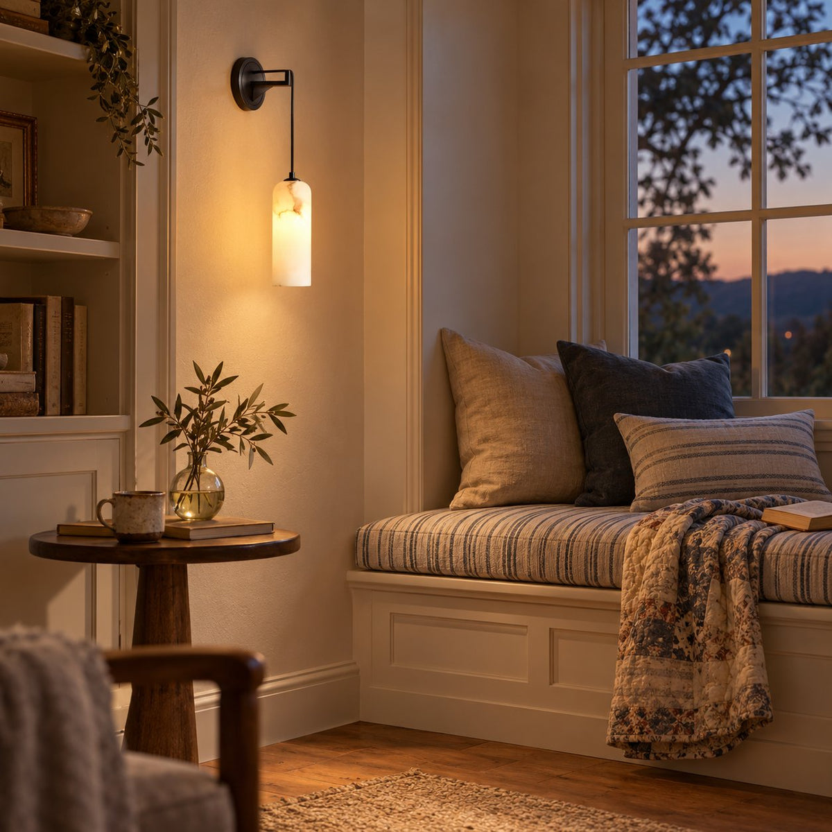 Zêzere black wall sconce with a marbled alabaster cylinder shade beside a window seat at dusk.