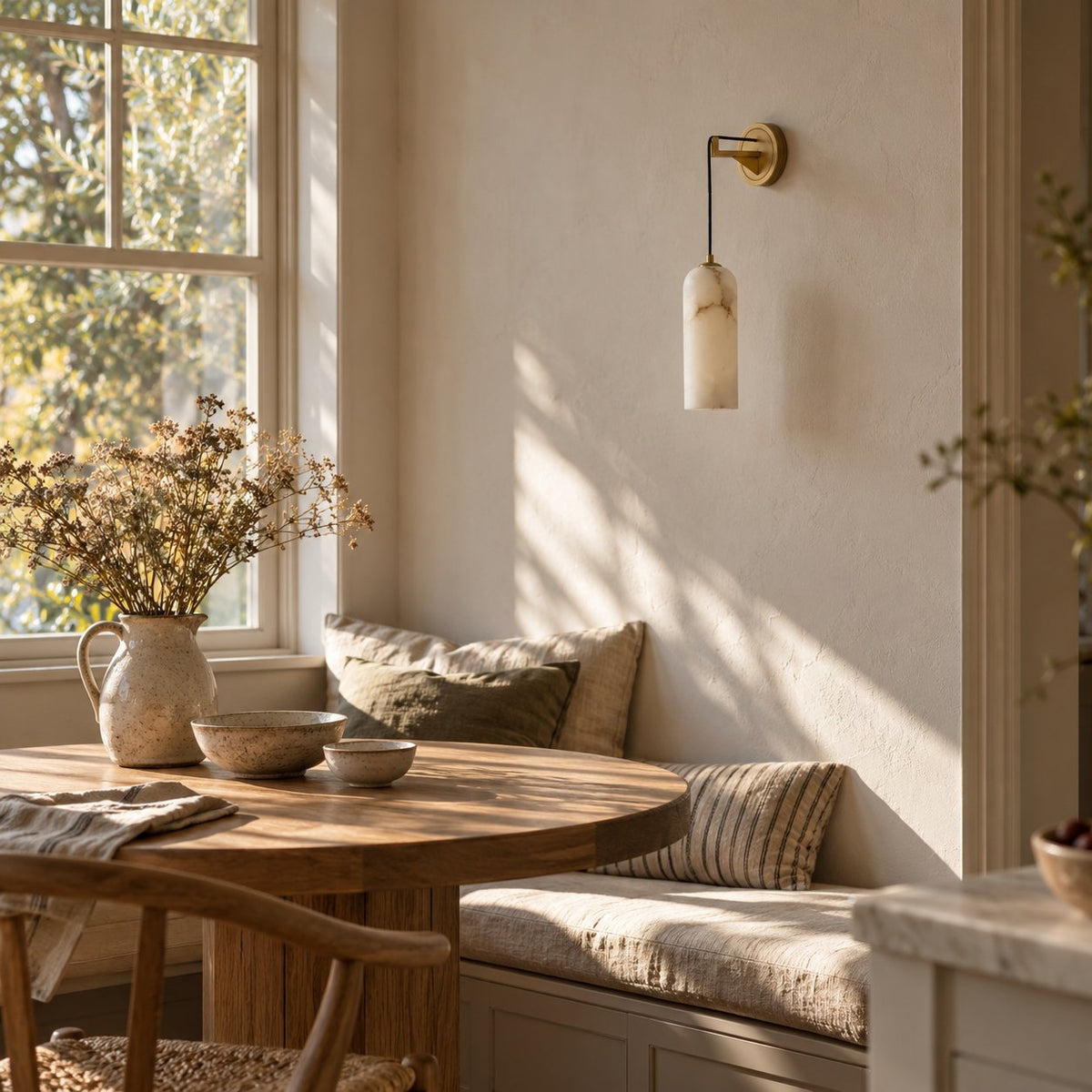 Zêzere alabaster wall sconce on a brass arm above a breakfast nook window seat.