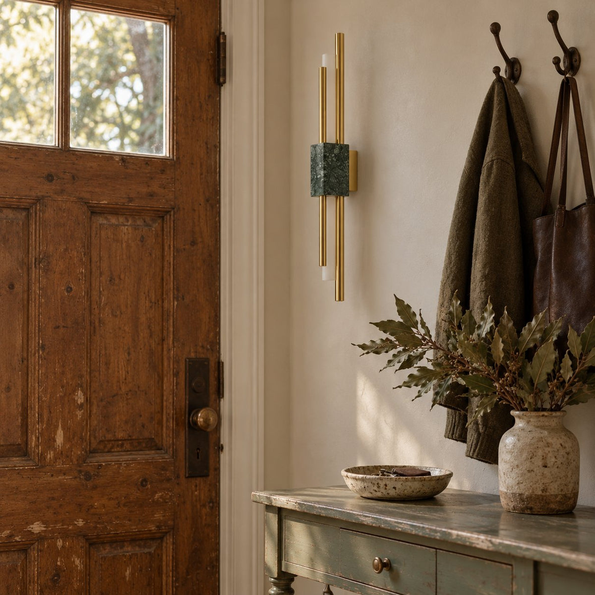 Alcochete asymmetric wall sconce with a green marble accent lit beside a wood entry door and coat hooks.