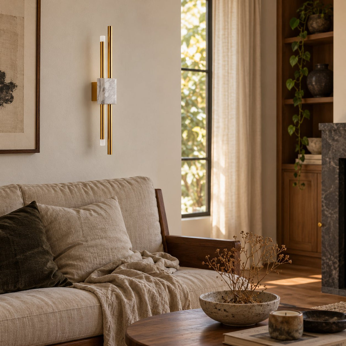 Alcochete white marble and gold wall sconce beside a linen sofa near a dark stone fireplace.