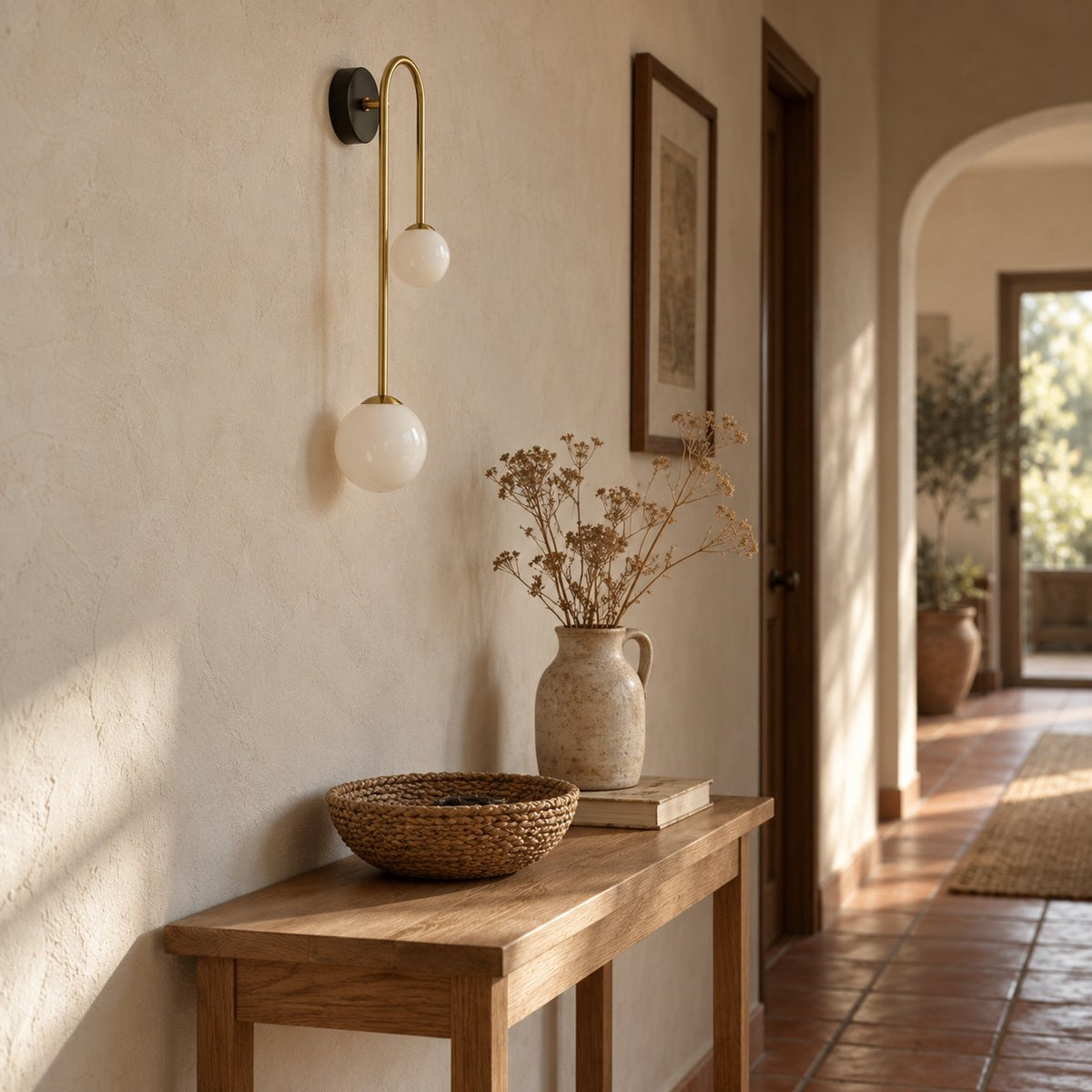 Alcoutim brass arc wall sconce with two glass globes above a console table in a hallway.