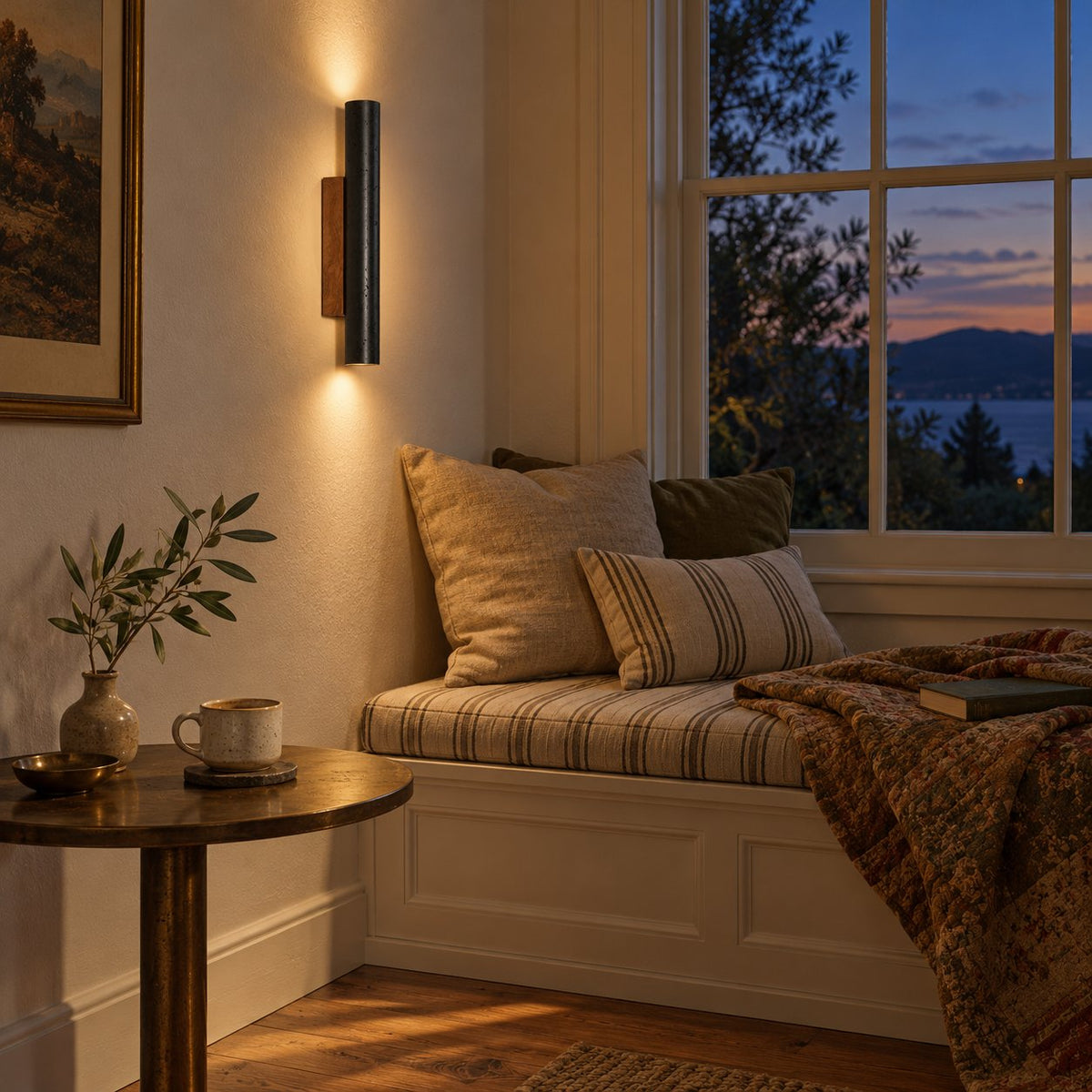 Arraiolos stone column sconce, black with a walnut mount, lit beside a window seat at dusk.