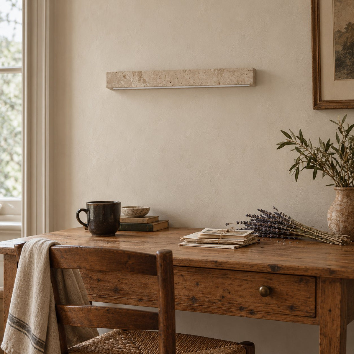 Barrancos travertine linear sconce above a wood desk with a sprig of lavender.