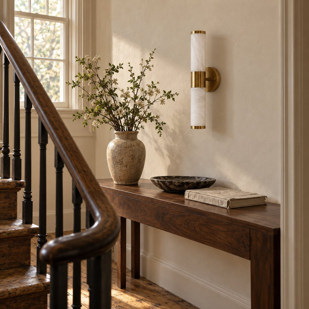 Beja alabaster wall sconce with brass bands above a console table near the stairs.