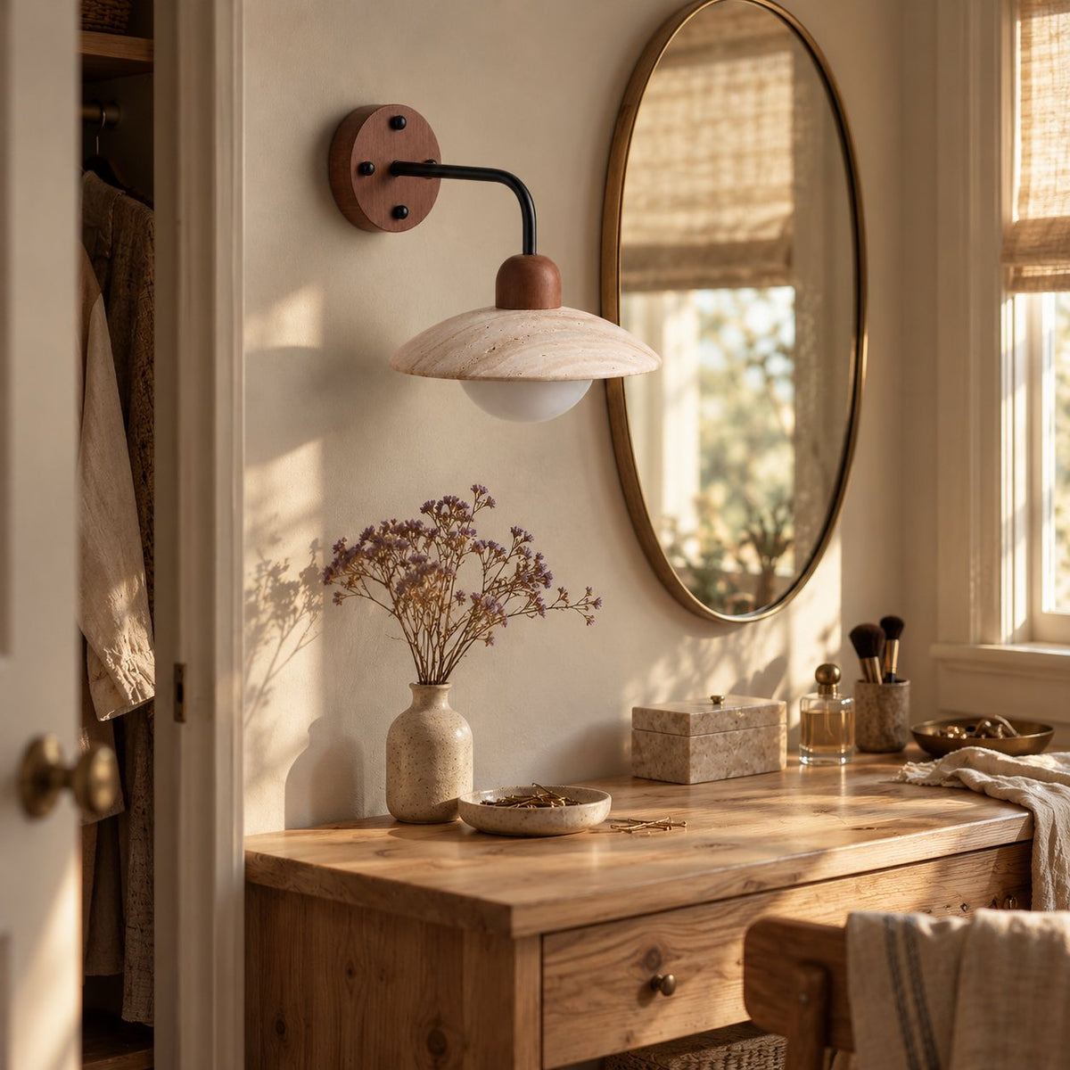 Boticas travertine dome arm sconce beside a round mirror on a bedroom dressing table.
