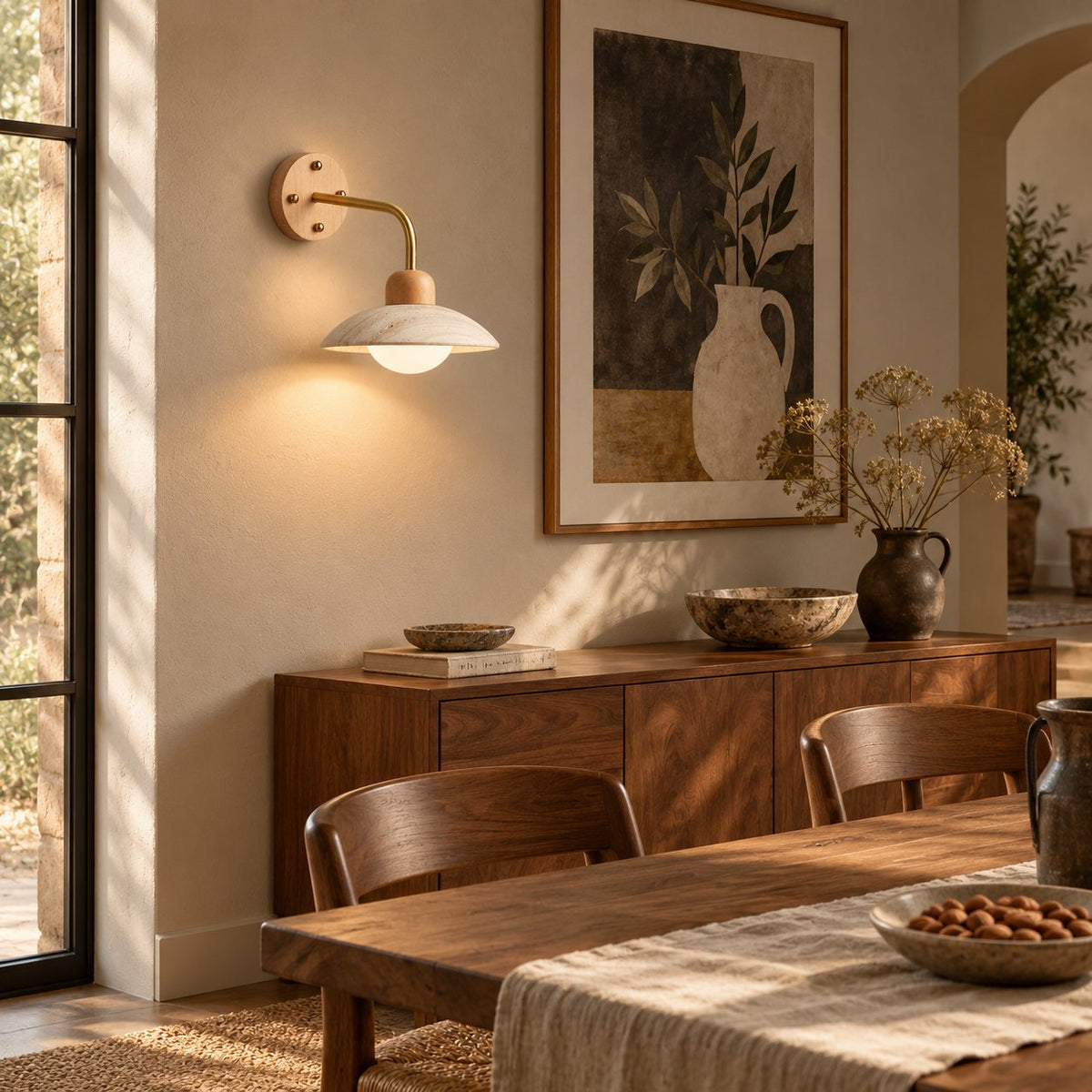 Boticas travertine dome arm sconce with a brass arm above a walnut dining sideboard.