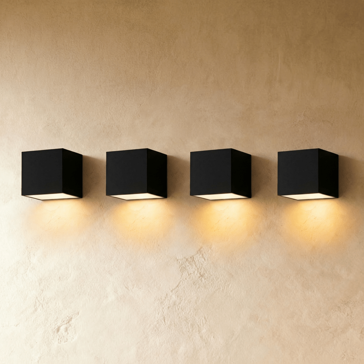 Row of four Clérachic black cube wall lights on a limewash plaster wall, each casting a warm pool of light below.