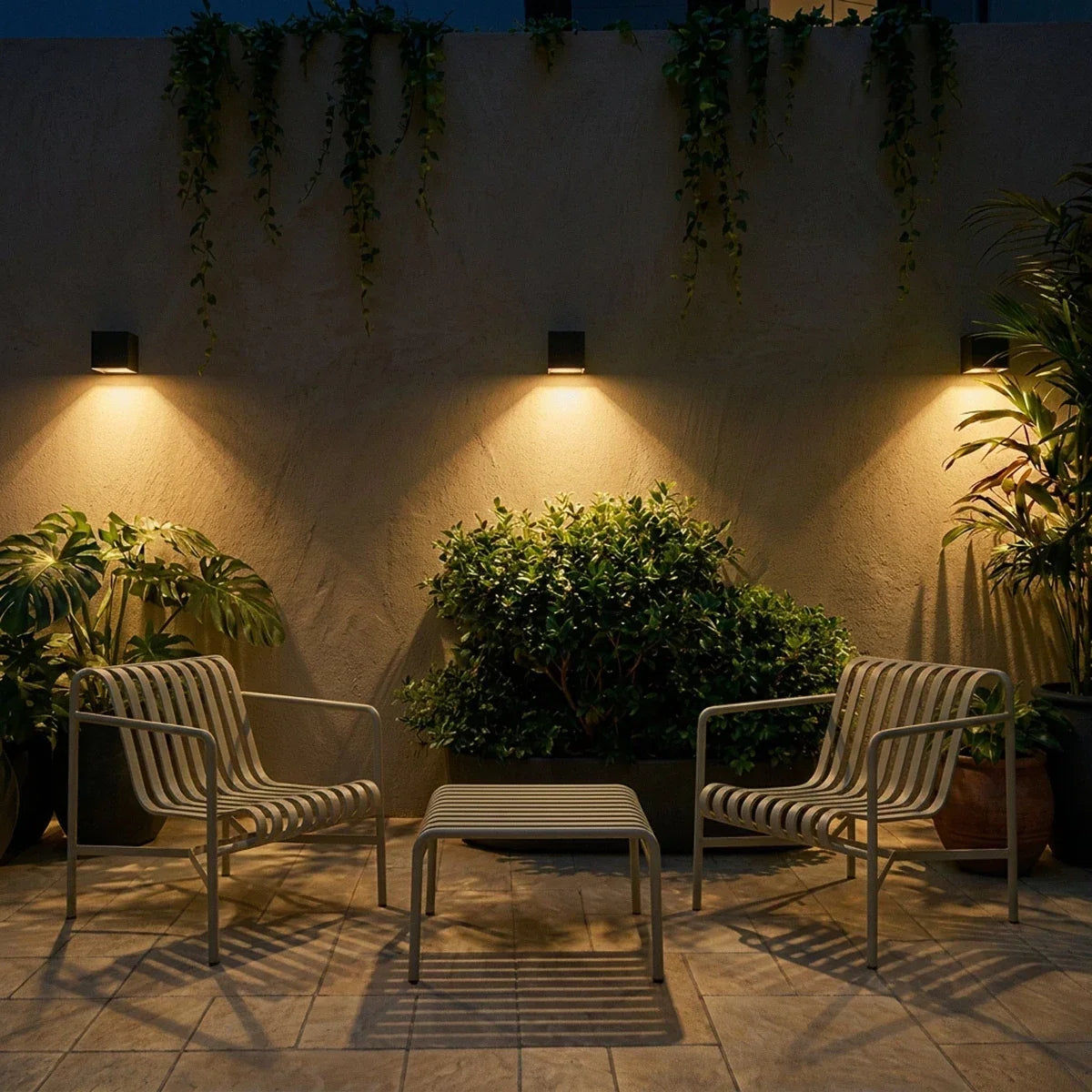 Clérachic black cube wall lights above a terrace seating area with two slatted chairs, lighting the wall and hanging vines.
