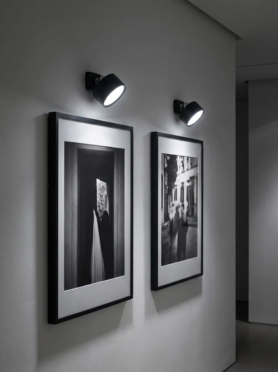 Two spotlights above framed black and white photographs on a gallery wall
