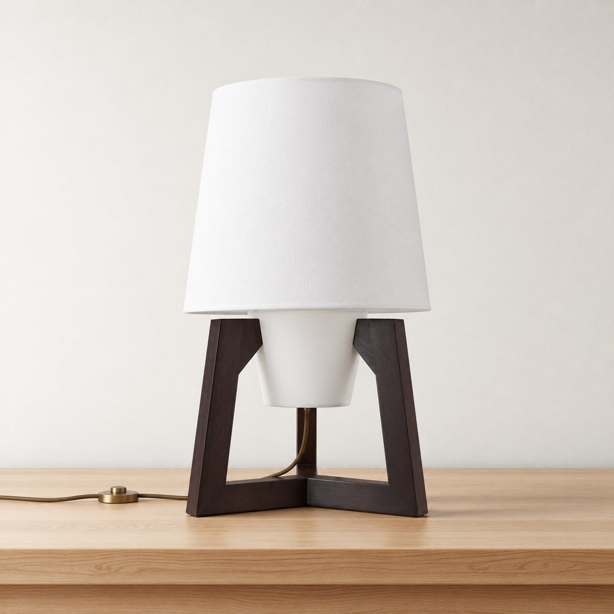 Morros small tripod linen lamp in black walnut, white linen shade on three short wooden legs, on an oak tabletop.