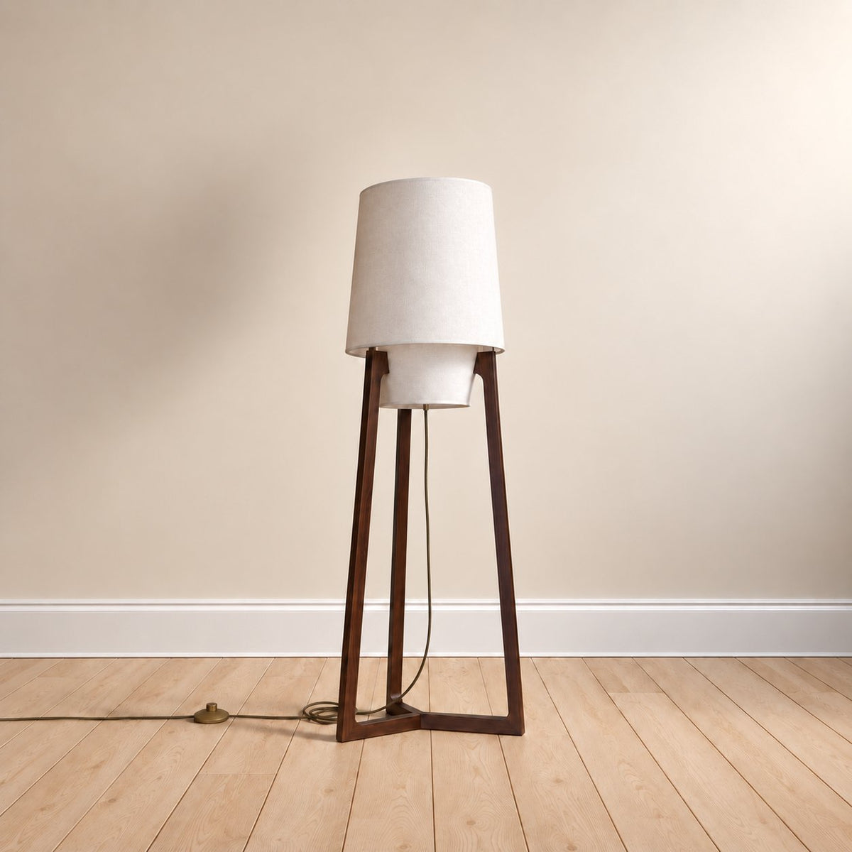 Morros tripod linen floor lamp in brown walnut, the 130 cm (51.2 in) size, cord to a brass foot switch, on an oak floor.