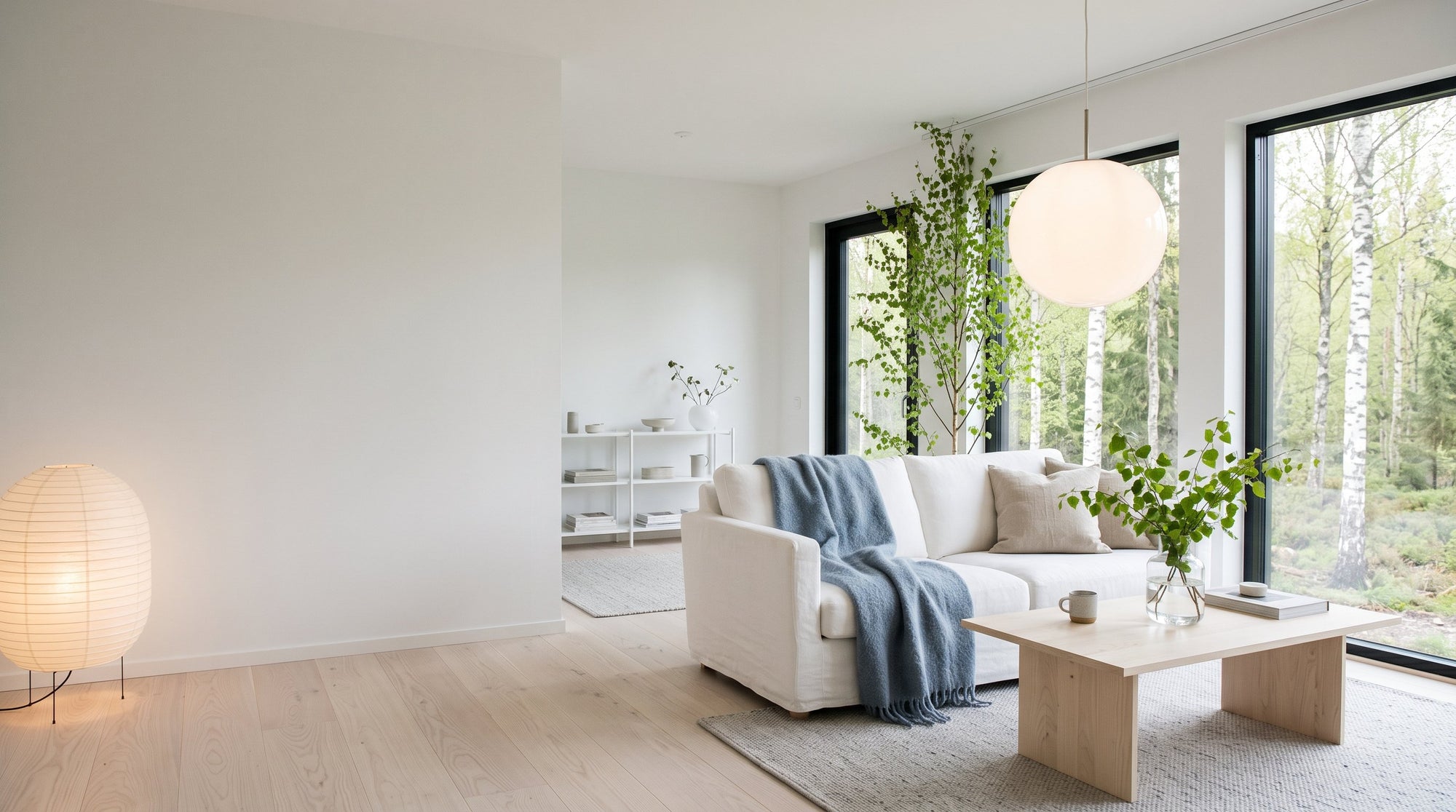 A bright Nordic living room with a white globe pendant, a paper floor lamp and birch trees outside