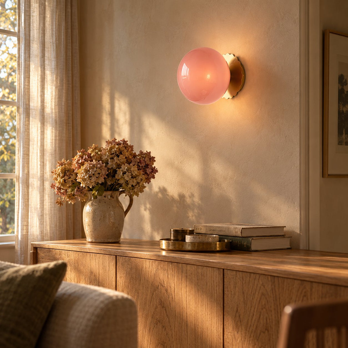 Tâmega convertible wall sconce in gold with pink glass, lit above an oak sideboard in a living room corner.
