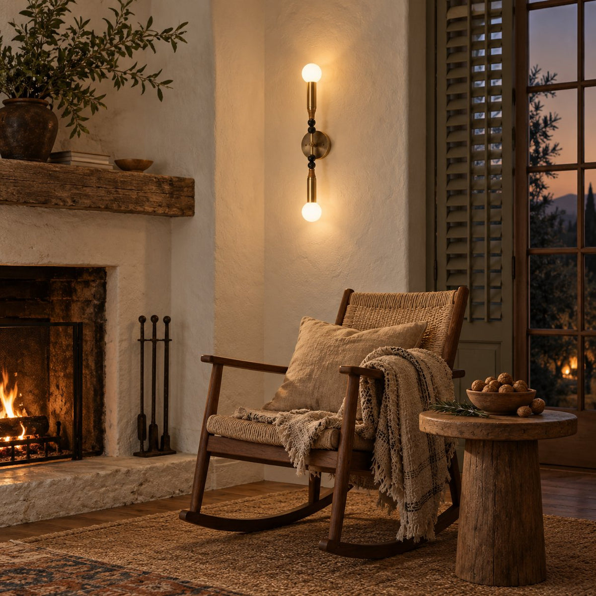 Torto brass double-globe wall sconce with black marble beads beside a fireplace and rocking chair.